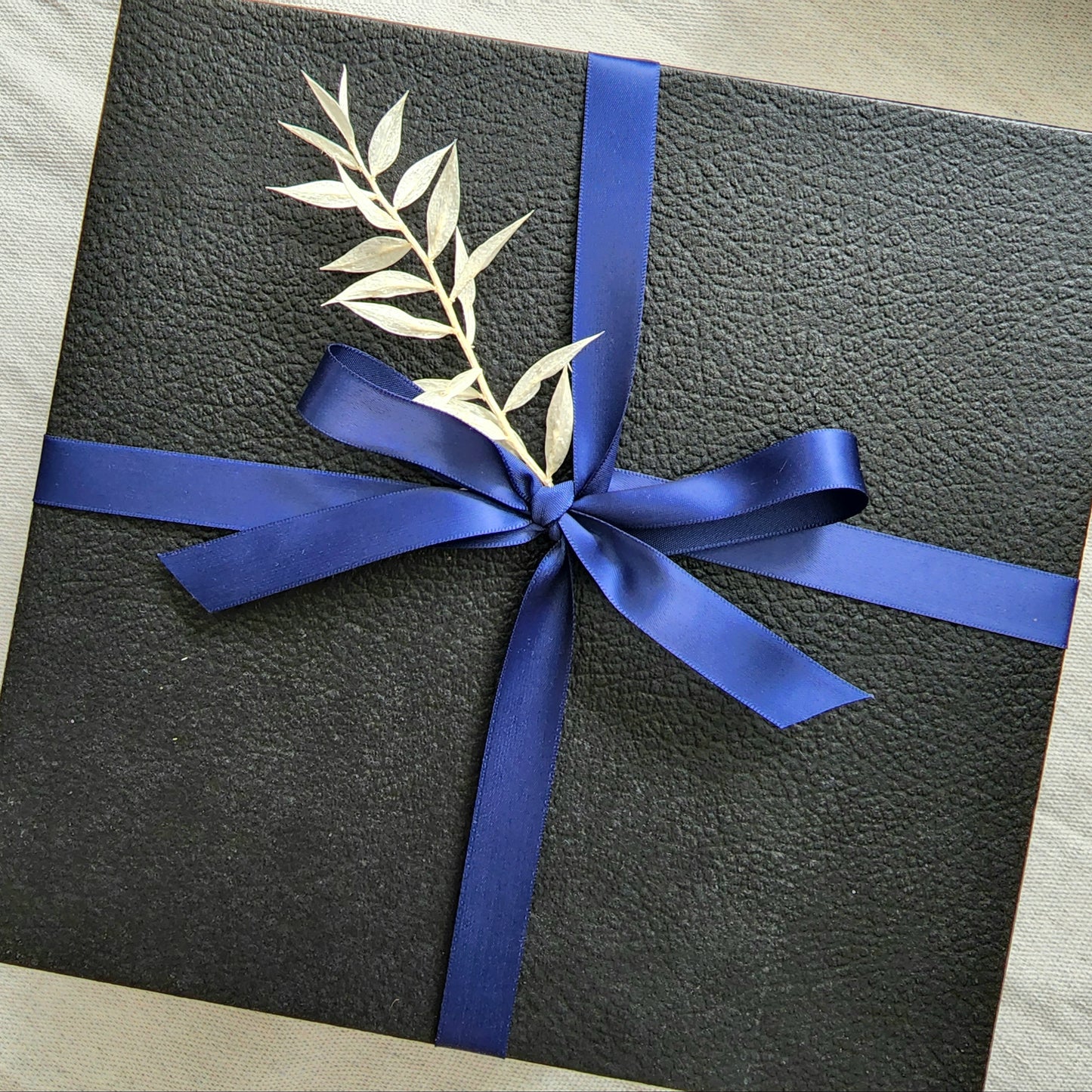 Embossed Black box with lid Wrapped in navy blue ribbon with white floral details.