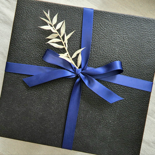 Embossed Black box with lid Wrapped in navy blue ribbon with white floral details.